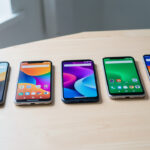 Les 5 meilleurs Samsung Galaxy à moins de 130 € en 2026 Plusieurs smartphones d’entrée de gamme alignés sur une table claire, avec des écrans allumés affichant des interfaces colorées abstraites dans une ambiance de comparatif high-tech.