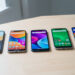 Plusieurs smartphones d’entrée de gamme alignés sur une table claire, avec des écrans allumés affichant des interfaces colorées abstraites dans une ambiance de comparatif high-tech.